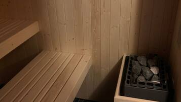 A wooden sauna with benches and a stone-filled container.