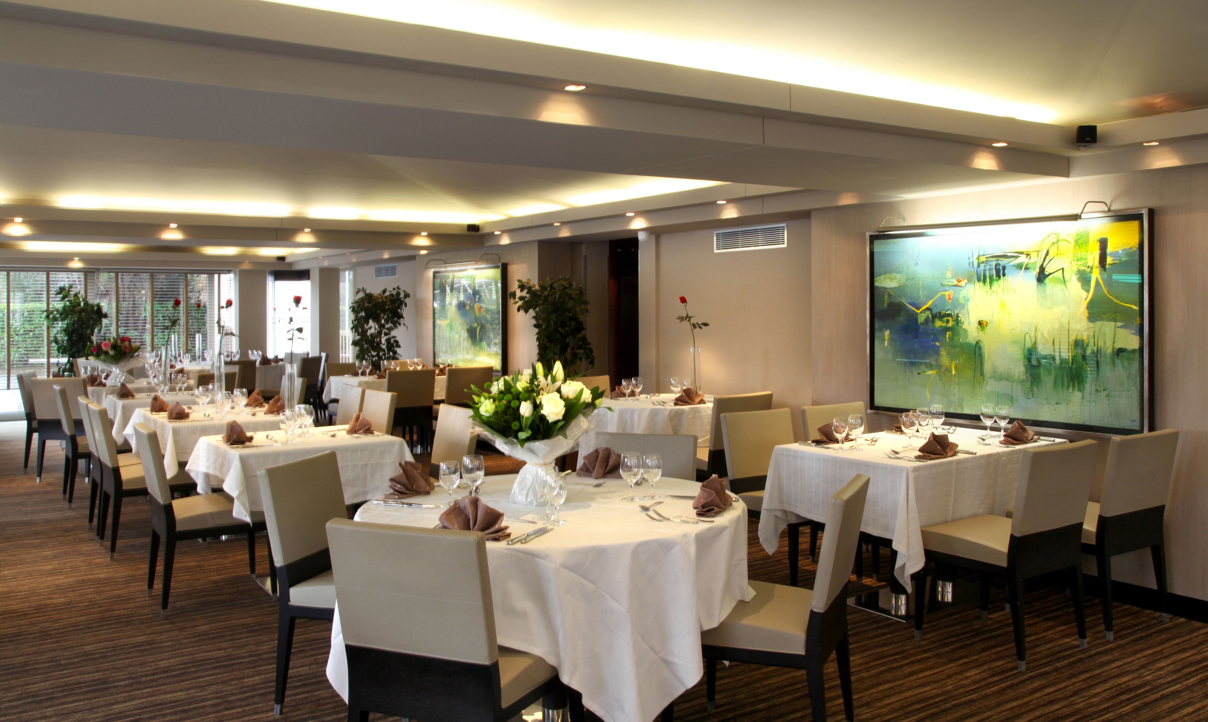 Een balzaal met meerdere ronde tafels gedekt voor een diner, elk met witte tafelkleden en stoelen.