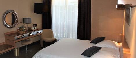 Habitación de hotel con cama, escritorio, silla, televisión y ventana con cortinas.
