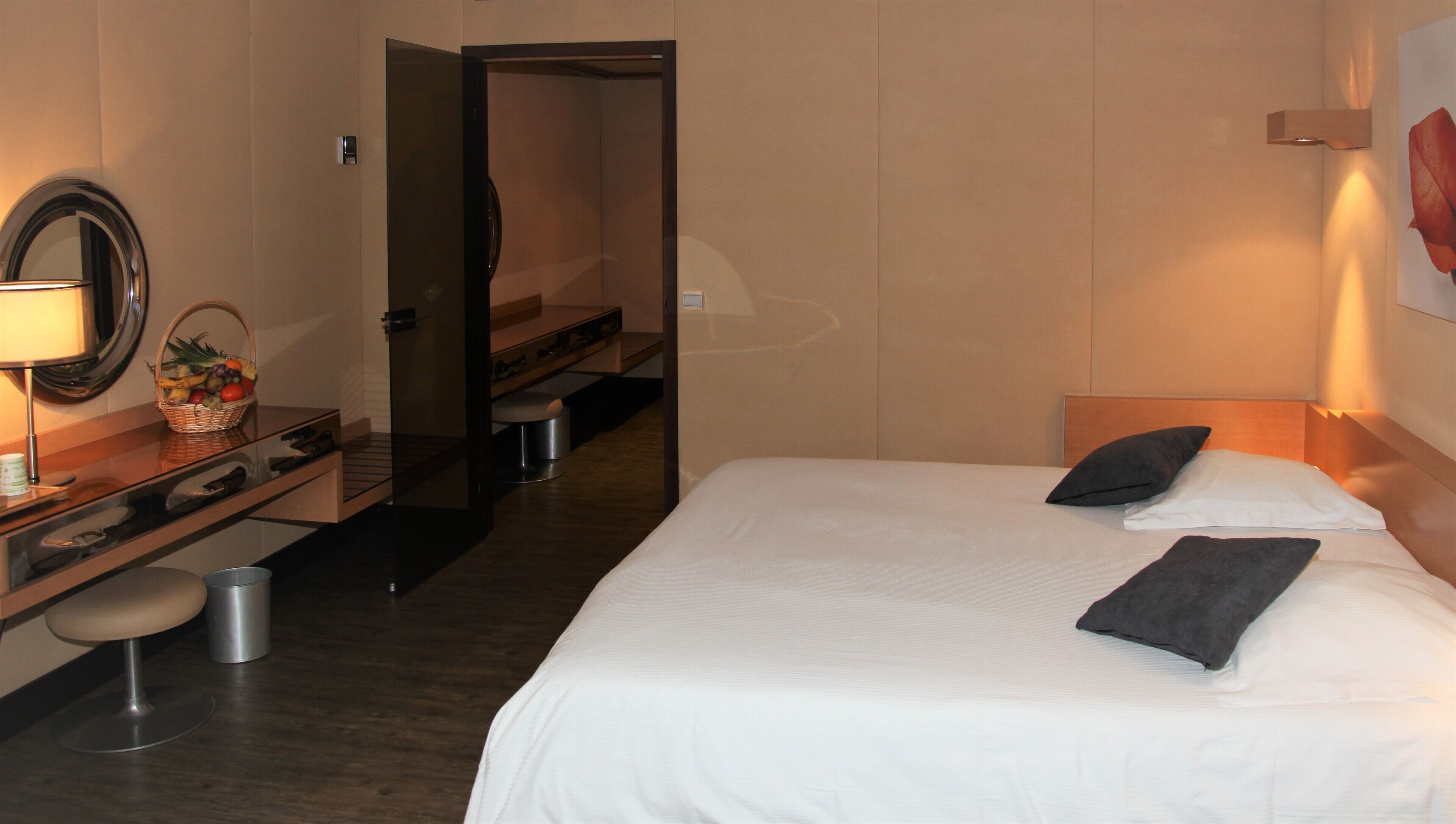 Quarto de hotel com cama, mesa de cabeceira, luminária e espelho.