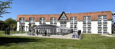 A hotel with a large glass structure in front, multiple balconies, and a well-maintained lawn.