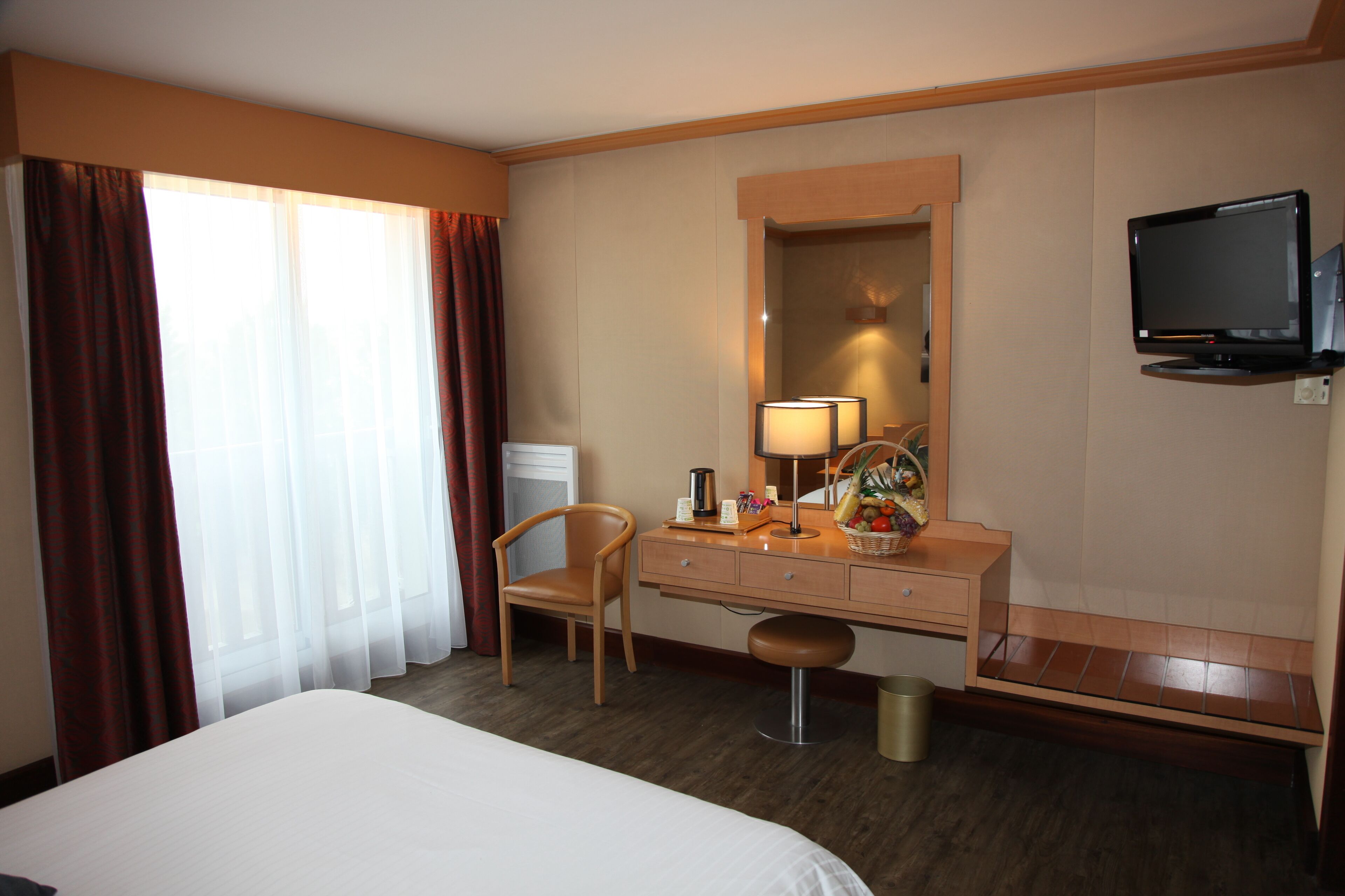 Ein Hotelzimmer mit einem Bett, einem Holztisch, einem Sessel, einem Fernseher und einem großen Fenster mit Vorhängen.