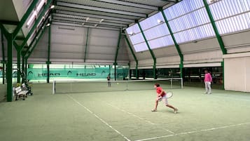 An indoor tennis court with a high ceiling and green structural beams.