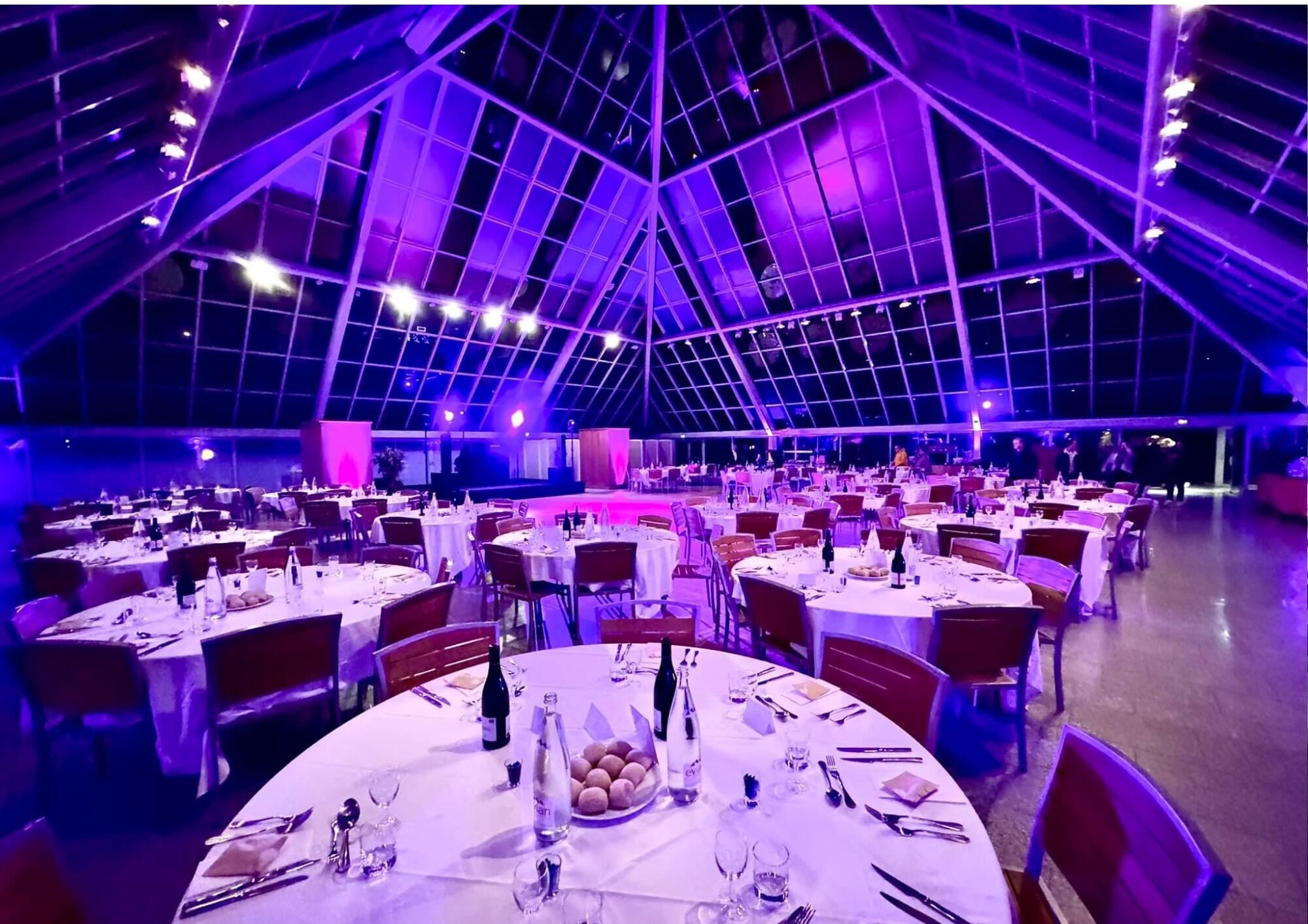 Un amplio espacio interior con varias mesas redondas dispuestas para comer, que cuenta con un techo alto y una estructura tipo entramado.