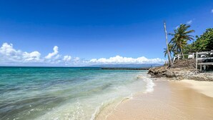 A beach with clear turquoise water, a sandy shore, and a stone pier extending into the sea.