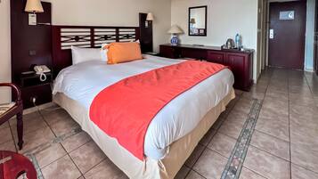 Una habitación de hotel con una cama grande, una mesita de noche con lámpara, un aparador y una puerta que da a otra habitación.
