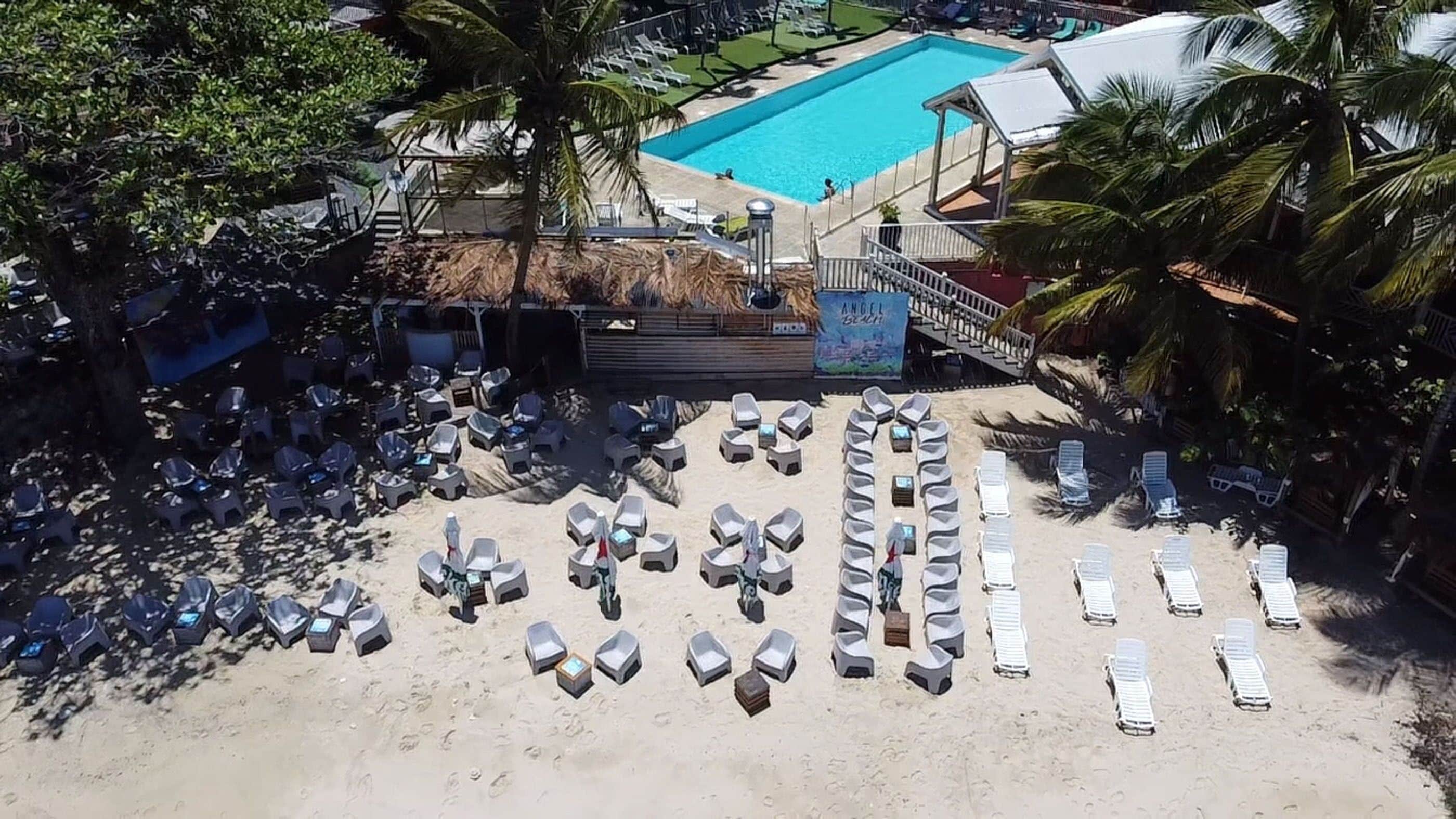 Un resort frente a la playa con piscina, sillas de descanso y palmeras.