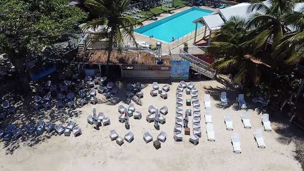 A beachside resort with a swimming pool, lounge chairs, and palm trees.