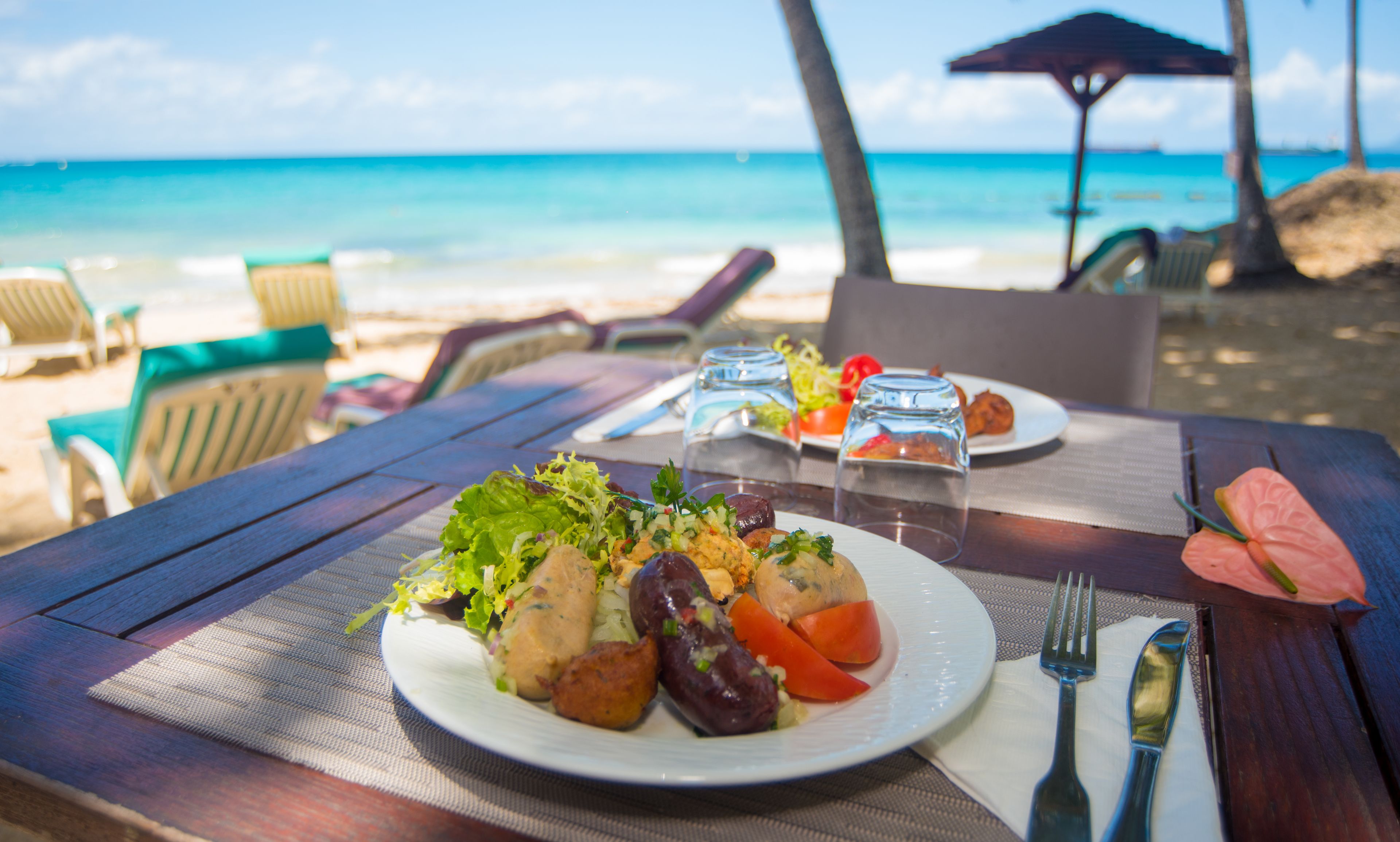 A table with a meal, a glass of water, and a fork and knife on a beach setting.