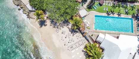 An aerial view of a beach resort with a swimming pool, sun loungers, and a beach area with umbrellas.