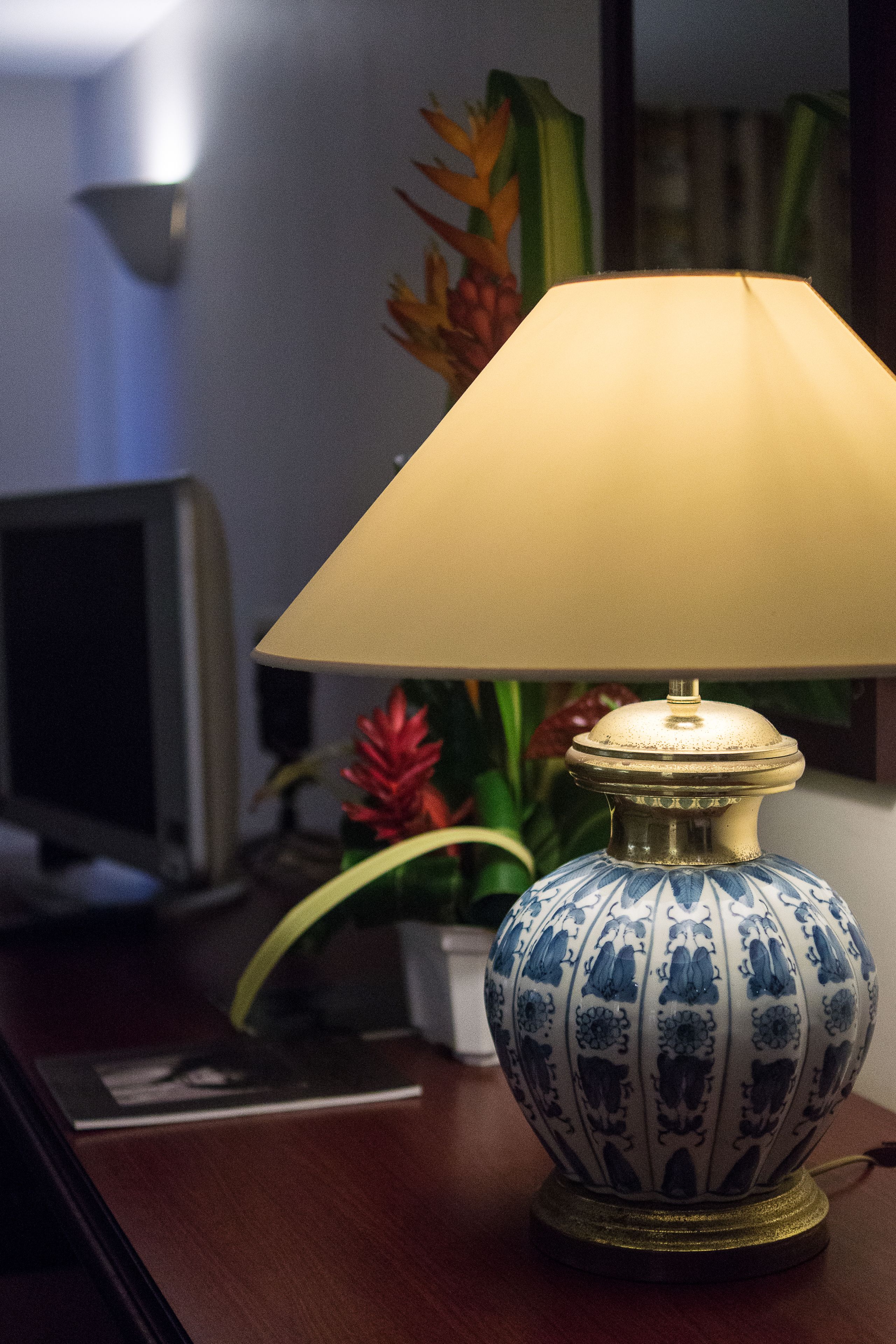 A table lamp with a blue and white patterned base and a beige lampshade, placed on a wooden desk.