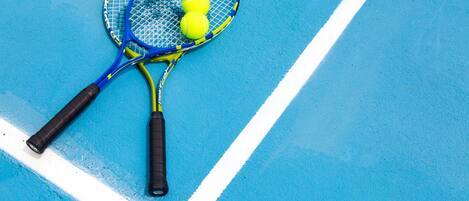 Two tennis rackets and three tennis balls on a blue tennis court.