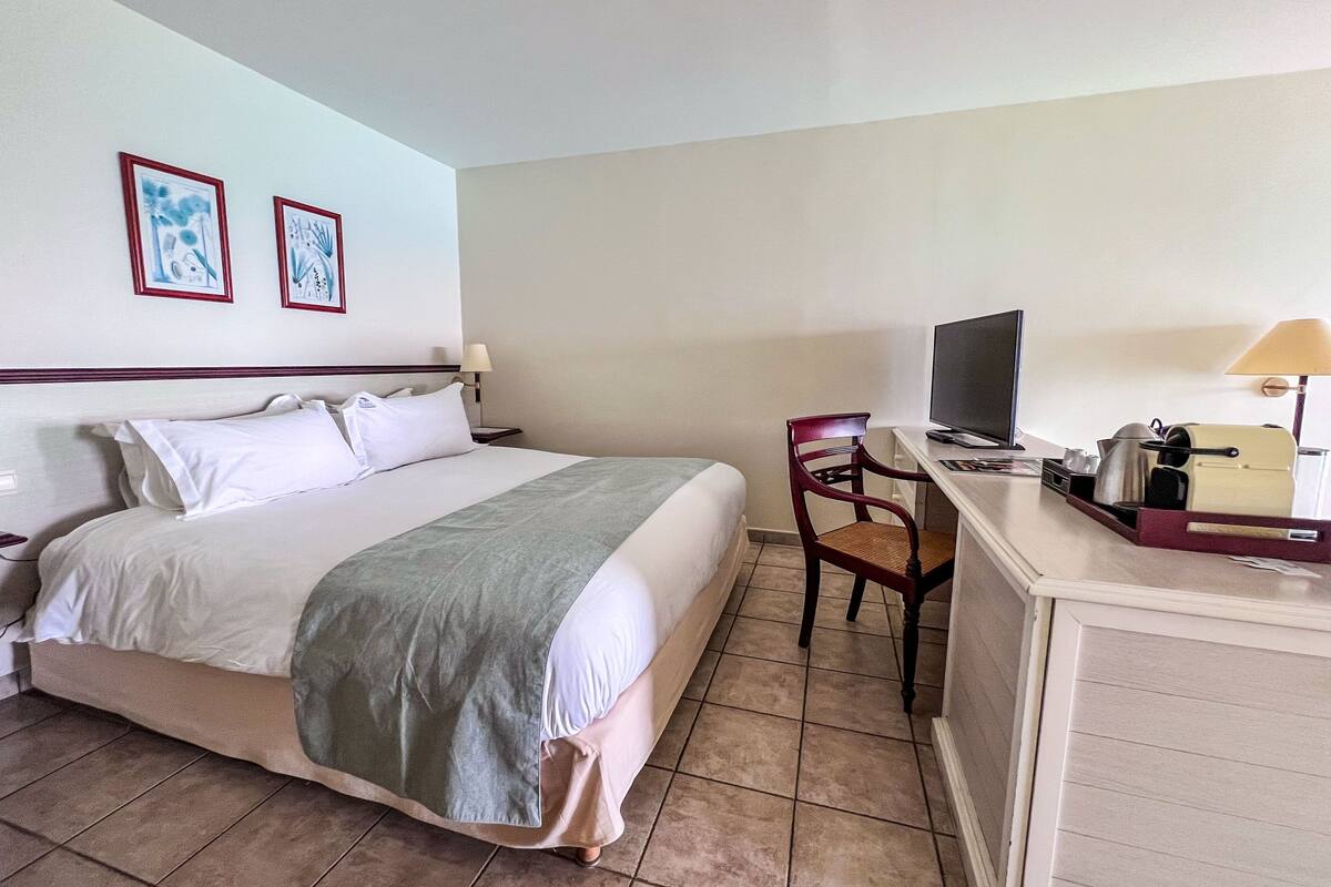 Une chambre d’hôtel avec un lit, un bureau équipé d’un ordinateur, une chaise et deux tableaux encadrés au mur.