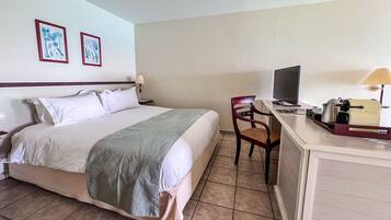 Een hotelkamer met een bed, een bureau met een computer, een stoel en twee ingelijste foto's aan de muur.