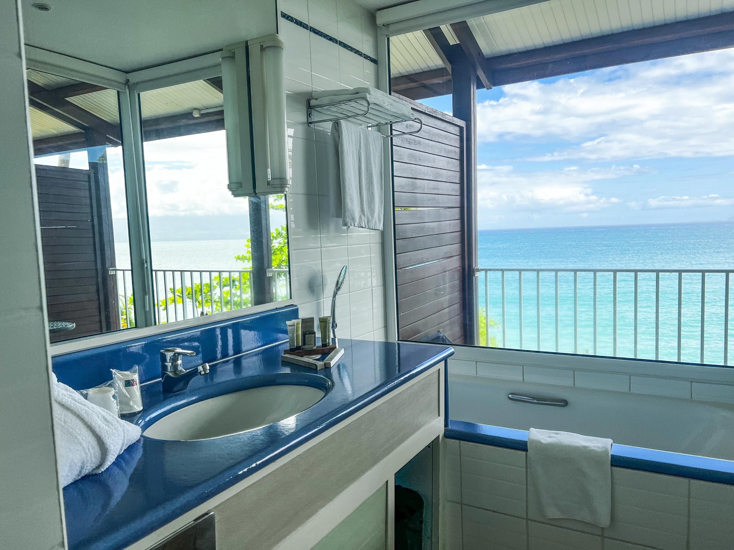 A bathroom with a blue sink, a mirror, and a view of the ocean.