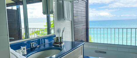 A bathroom with a blue sink, a mirror, and a view of the ocean.