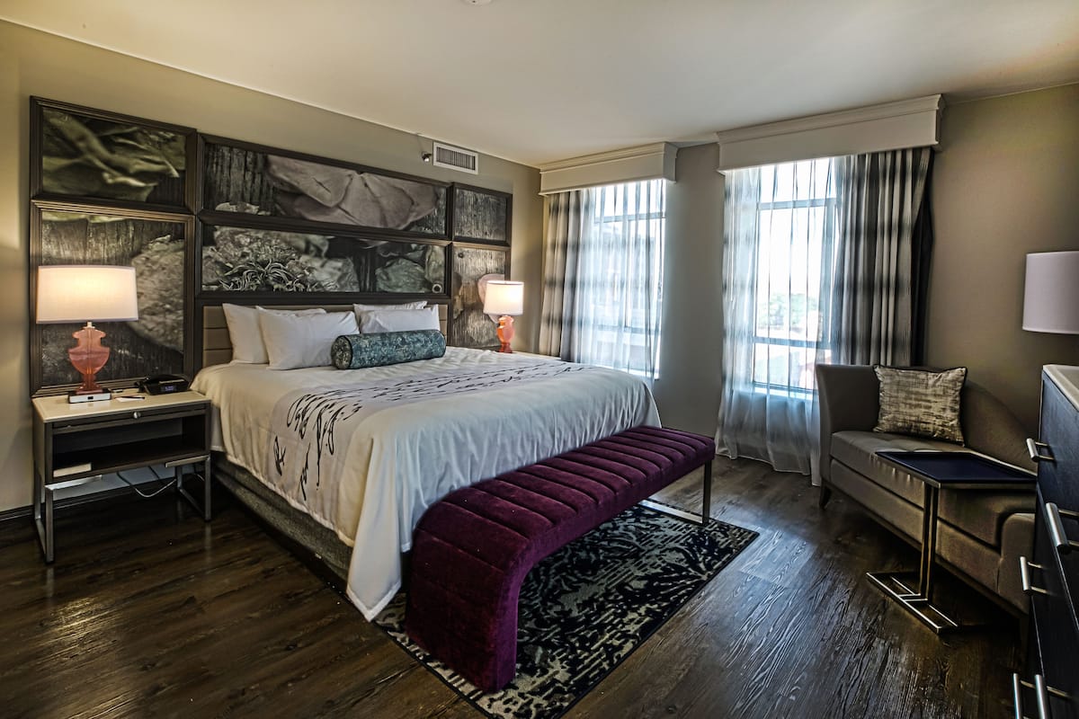 A modern hotel room with a large bed, a bench, a sofa, and a desk.