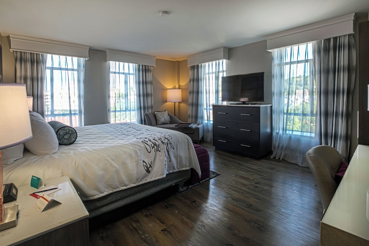 Une chambre d’hôtel avec un grand lit, un bureau avec une lampe, une commode, une télévision et une chaise.