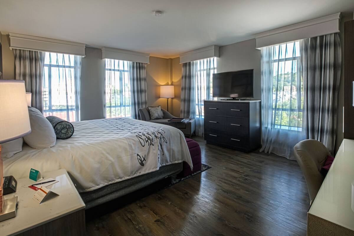 A hotel room with a large bed, a desk with a lamp, a TV, and a dresser.