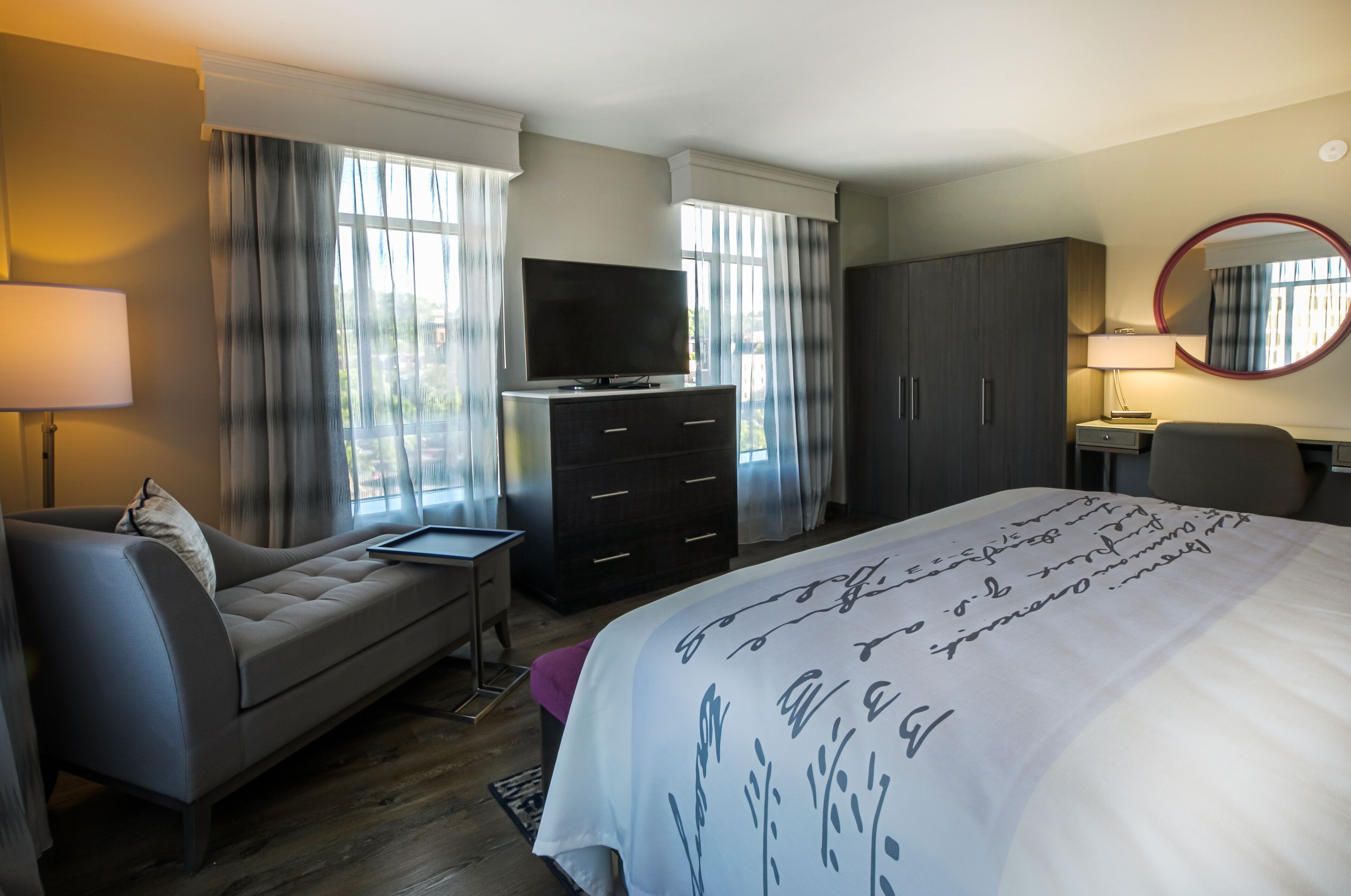 A hotel room with a bed, a sofa, a TV, a dresser, and a desk with a lamp.