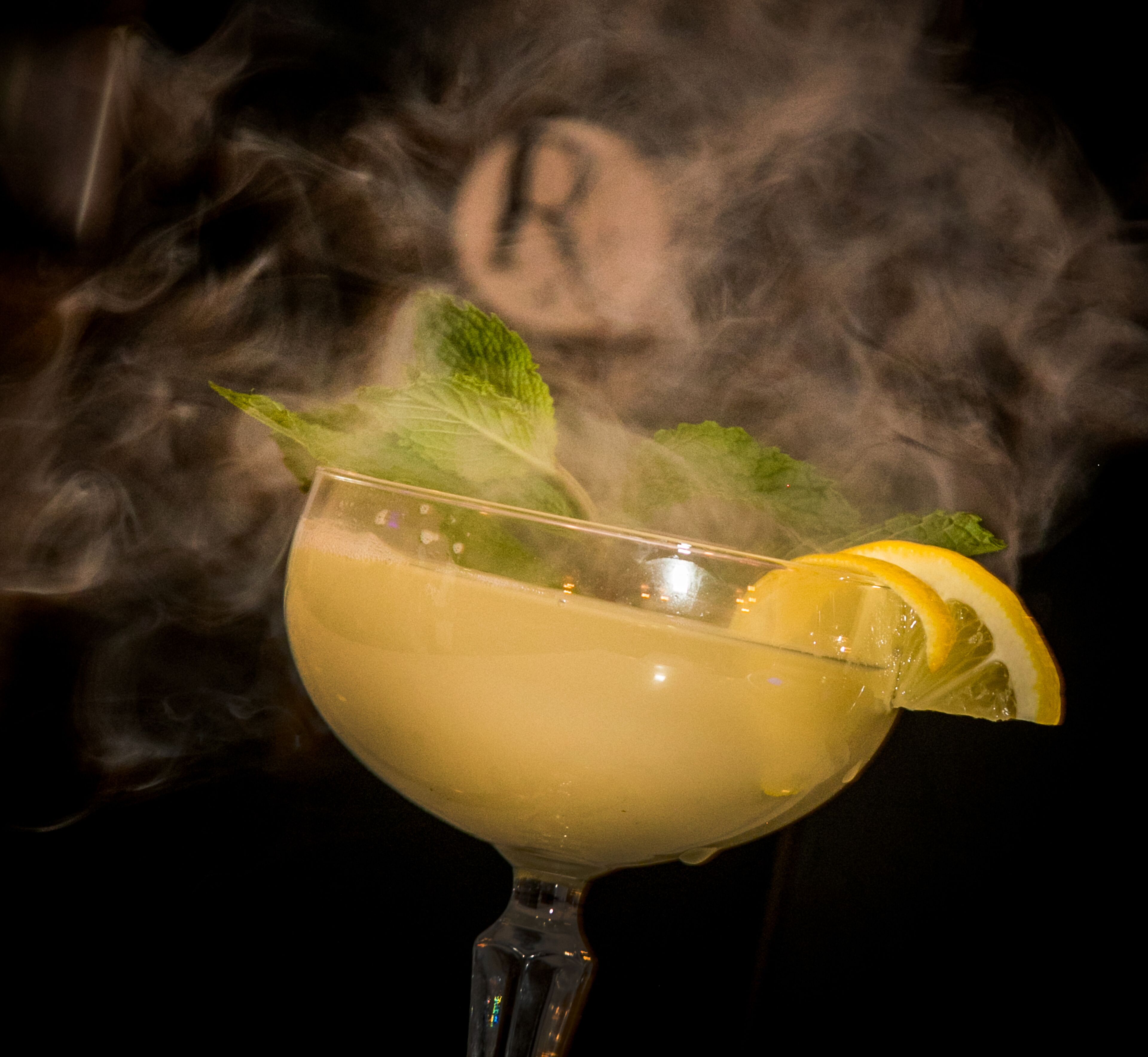A cocktail with a lemon slice and mint leaves, surrounded by smoke.
