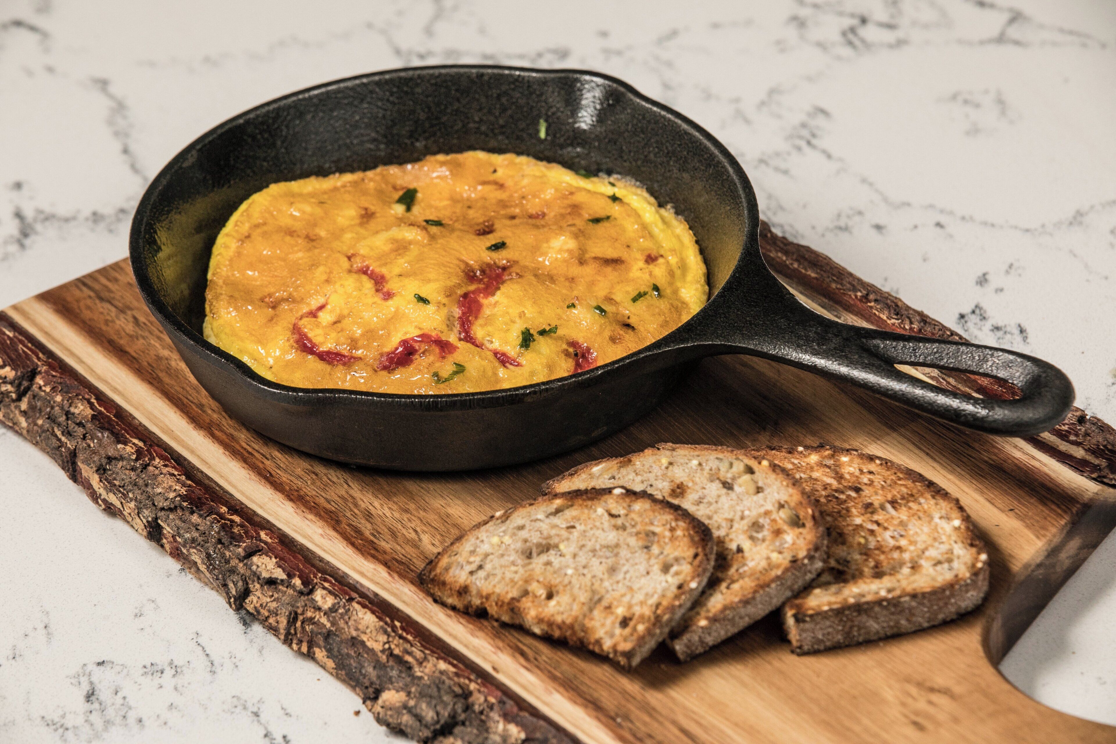 A skillet with a dish on a wooden board, accompanied by slices of bread.