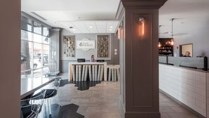 Zona de recepción de hotel con diseño moderno, que incluye mostrador de recepción, área de estar y un ventanal con vistas al exterior.