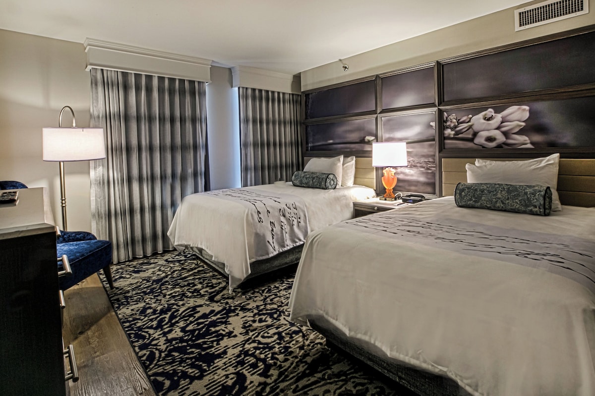 Une chambre d’hôtel avec deux lits, un bureau, une lampe et un grand panneau décoratif mural.