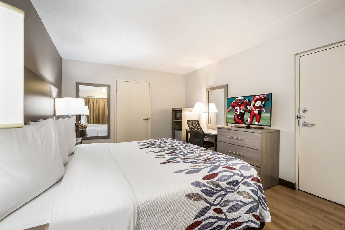 A hotel room with a bed, a desk, a chair, a television, and a wardrobe.
