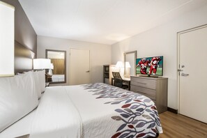 A hotel room with a bed, a desk, a chair, a television, and a wardrobe. - Red Roof Inn Lansing West - MSU (Lansing)