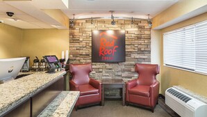 A reception area with a stone wall, two leather chairs, a reception desk, and a sign that reads 'Red Roof Inn.' - Red Roof Inn Lansing West - MSU (Lansing)