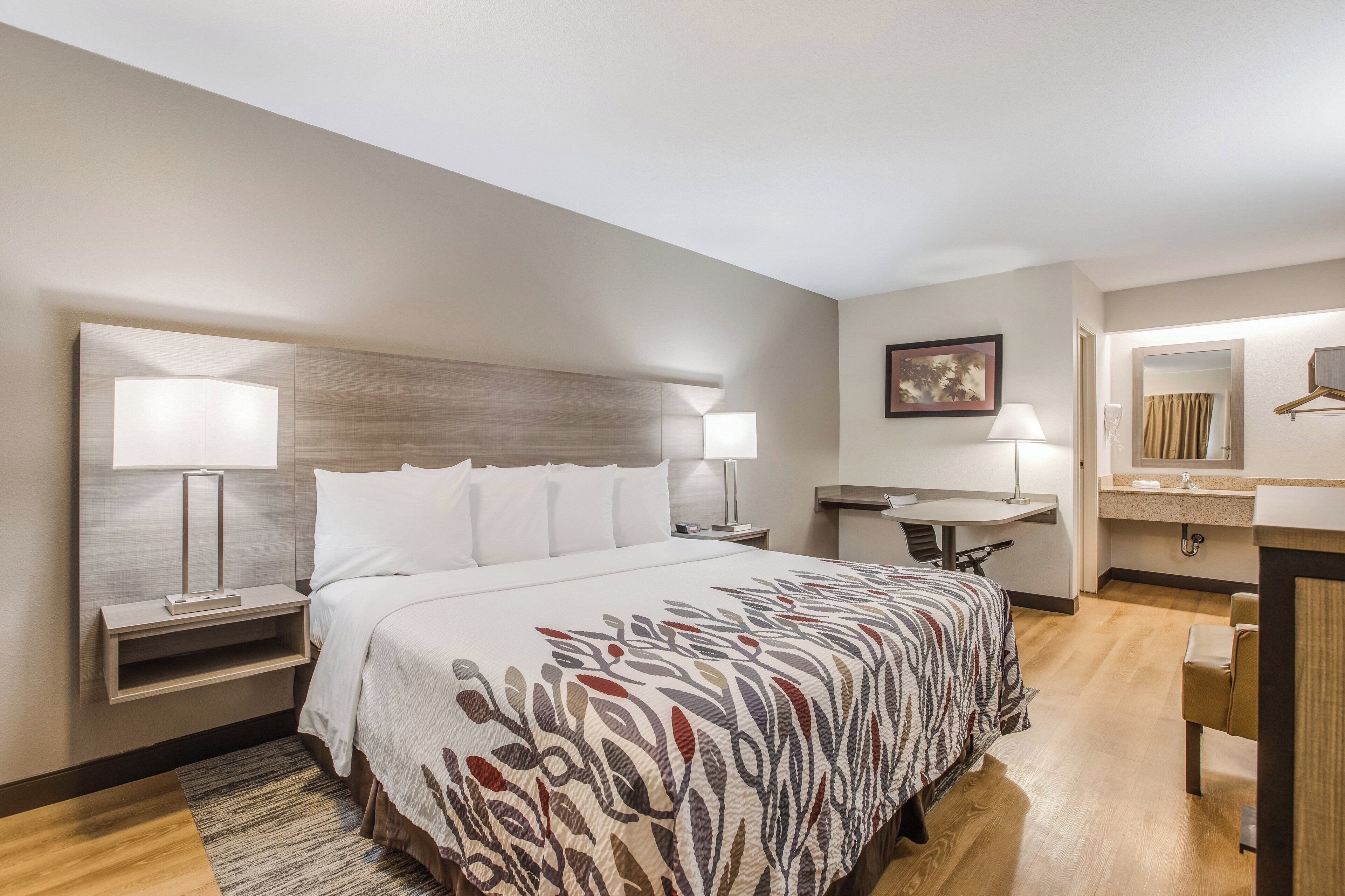 A hotel room with a bed, bedside tables, a desk, a chair, a mirror, and a bathroom.