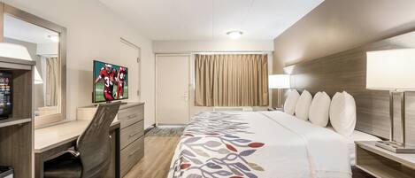 Habitación de hotel con cama, escritorio, silla, televisor y ventana con cortinas.