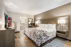 A hotel room with a large bed, a television, a desk, and a bathroom visible through an open door. - Red Roof Inn Lansing West - MSU (Lansing)