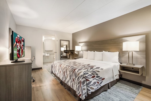 A hotel room with a large bed, a television, a desk, and a bathroom visible through an open door.