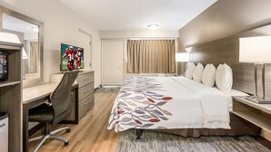 A hotel room with a bed, desk, chair, TV, and curtains. - Red Roof Inn Lansing West - MSU (Lansing)