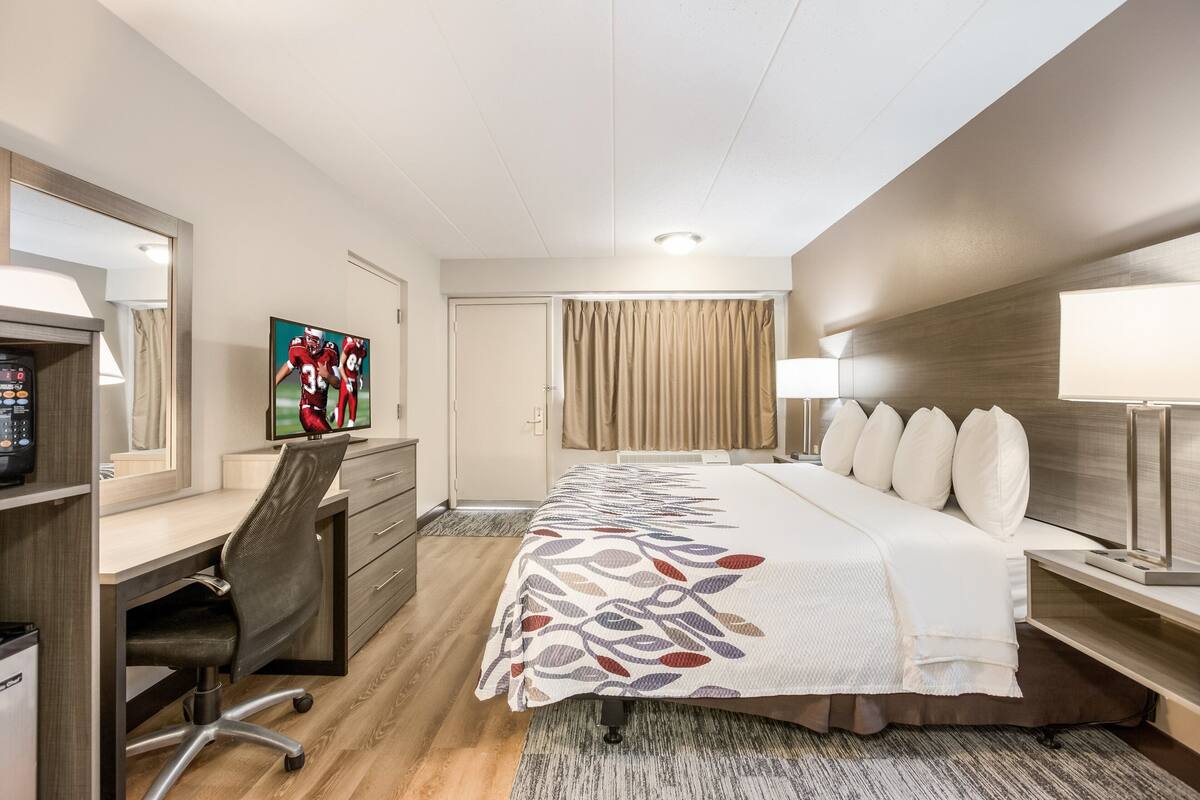A hotel room with a bed, desk, chair, TV, and curtains.
