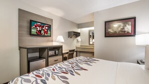 A hotel room with a bed, a desk with a computer, a TV, a mirror, and a framed picture on the wall. - Red Roof Inn Lansing West - MSU (Lansing)