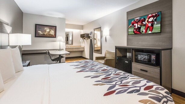 A hotel room with a bed, a desk, a television, and a bathroom visible through an open door. - Red Roof Inn Lansing West - MSU (Lansing)