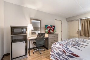 A hotel room with a bed, a desk with a computer, a microwave, a refrigerator, a TV, and a door with curtains. - Red Roof Inn Lansing West - MSU (Lansing)
