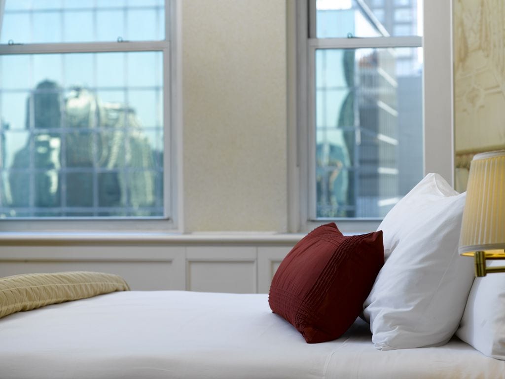 Ett hotellrum med en säng, två fönster och utsikt över stadsbilden.