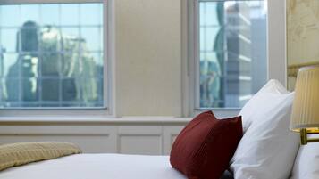 A hotel room with a bed, two windows, and a view of the cityscape.