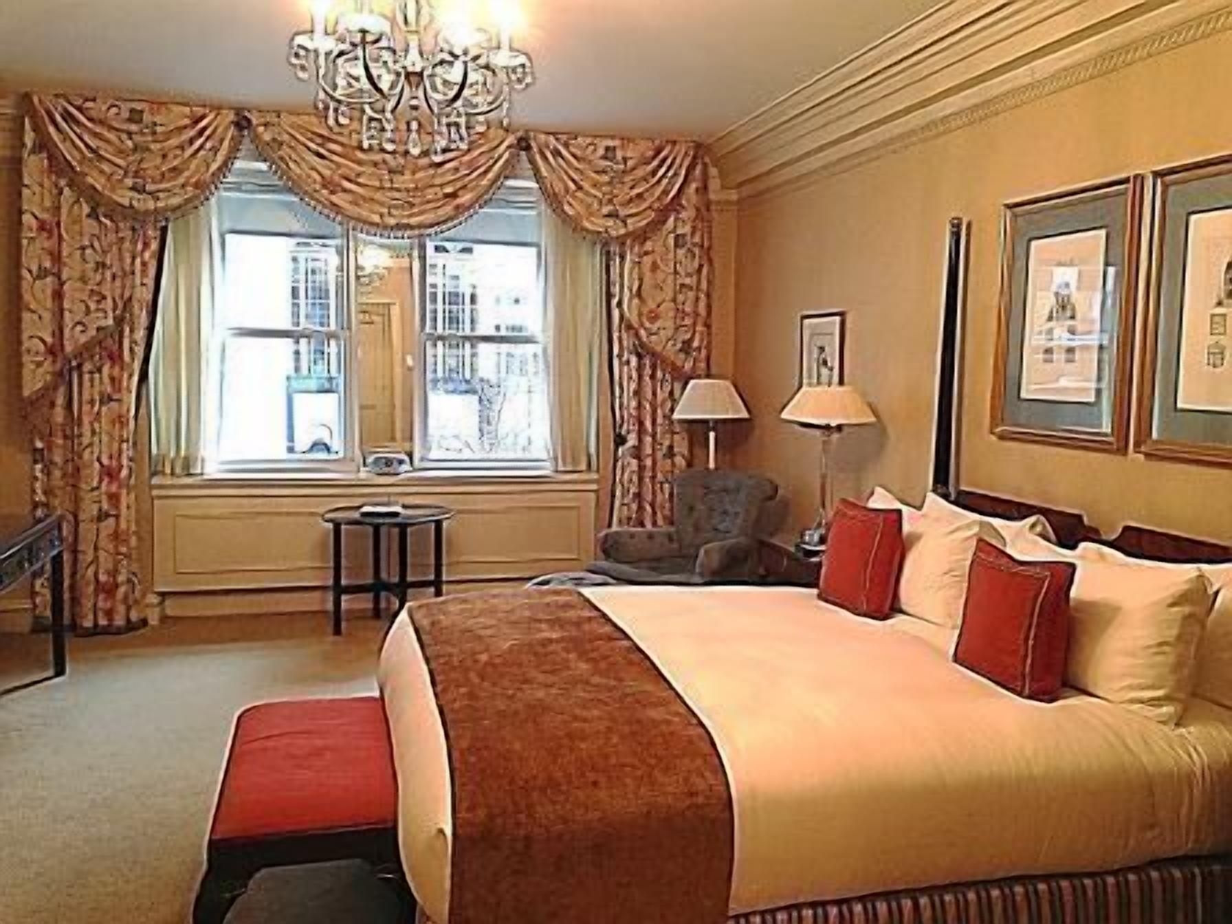 A hotel room with a large bed, a chandelier, a window with curtains, a small table, and framed pictures on the wall.