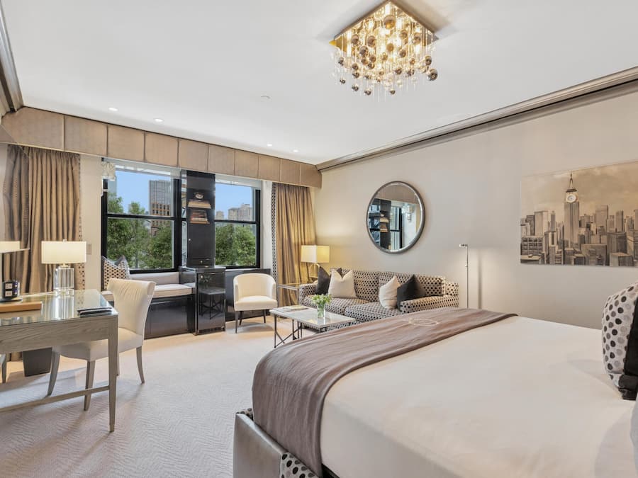 Ett modernt hotellrum med en stor säng, ett skrivbord, en soffa och en tavla som föreställer en stadsbild.