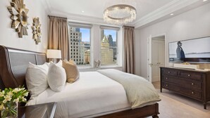 A spacious bedroom with a large bed, a television, and a view of the cityscape through large windows. - The Sherry Netherland (New York)