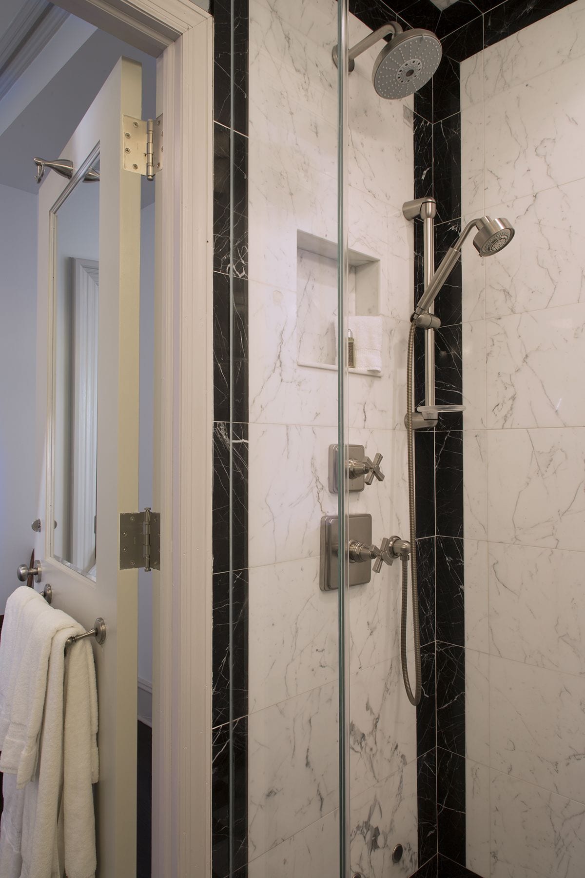 A bathroom with a glass-enclosed shower, marble walls, and a towel rack with towels.