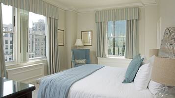 A hotel room with a large bed, a chair, a desk, and a lamp.