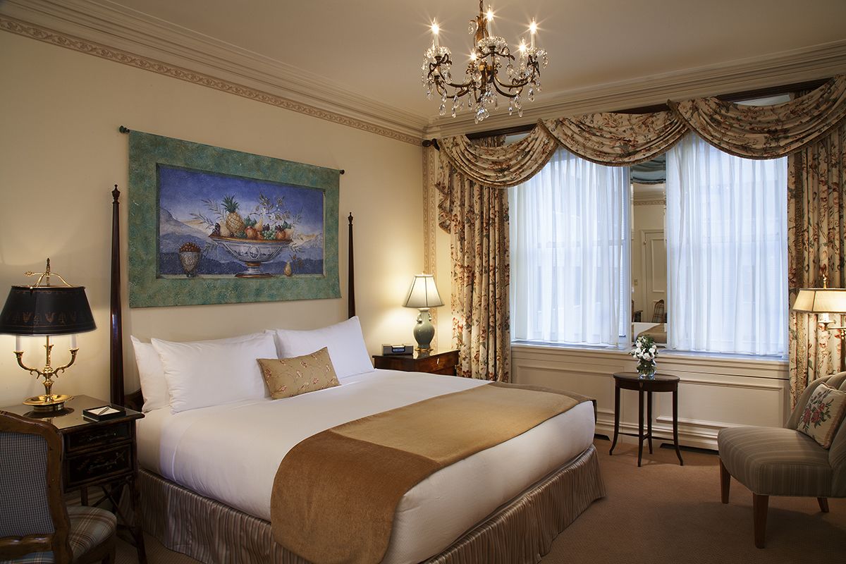 A hotel room with a large bed, a chandelier, a painting, and curtains.
