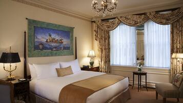 A hotel room with a large bed, a chandelier, a painting, and curtains.
