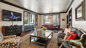 A modern living room with a large flat-screen TV, a patterned sofa, a coffee table, and a dining area with red chairs. - The Sherry Netherland (New York)